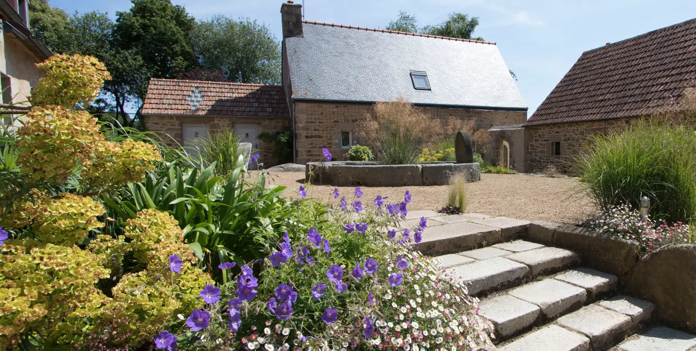 Aménagement paysager avec jardin fleuri et pavés devant une maison traditionnelle en pierre dans le Trégor, réalisé par les Établissements Rochelle, paysagiste à Lannion.